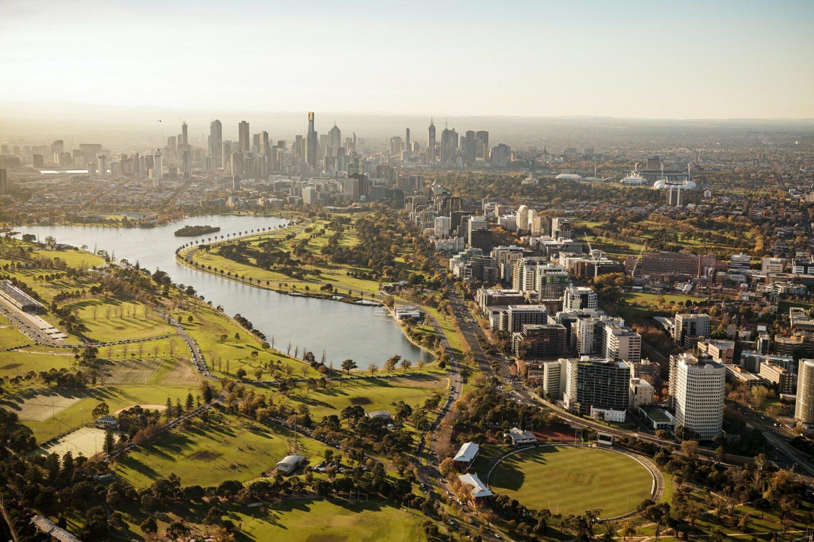 Lush city park with a river, high-rise buildings, and skyline in Melbourne, Australia.